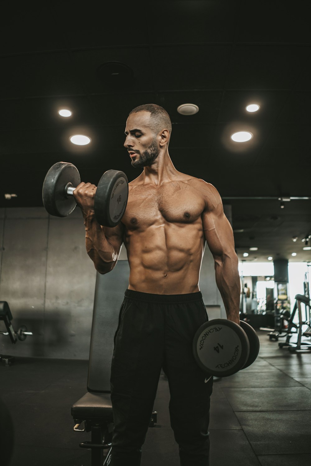 a shirtless man holding a dumbbell in a gym