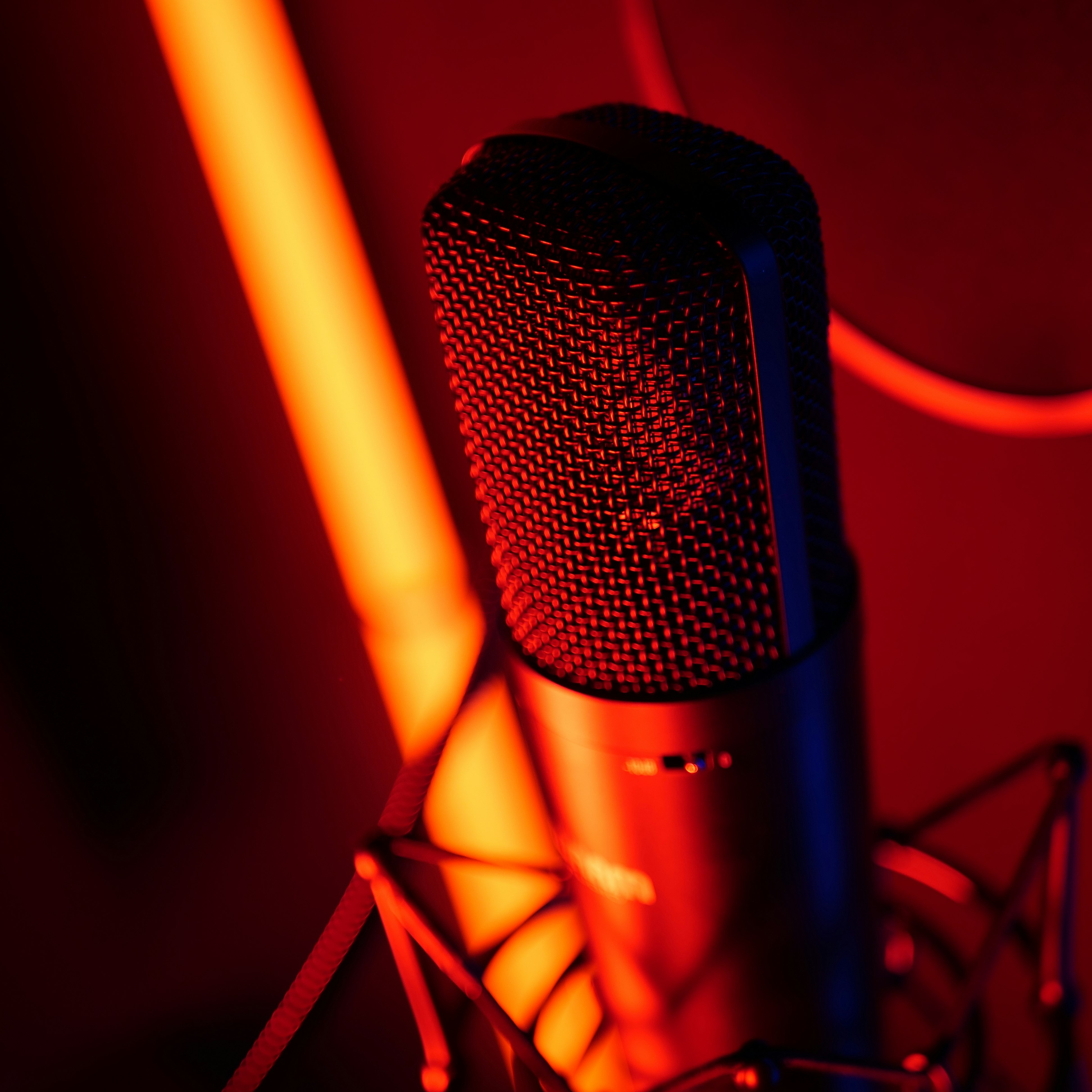 View of a microphone in the booth of a recording studio with red neon light.