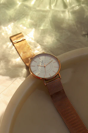 Elegant gold-tone watch with a white dial displayed on a marble surface.