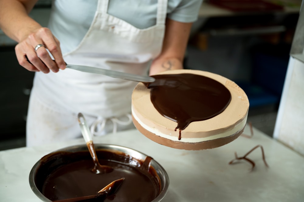 a woman in an apron is spreading chocolate on a cake