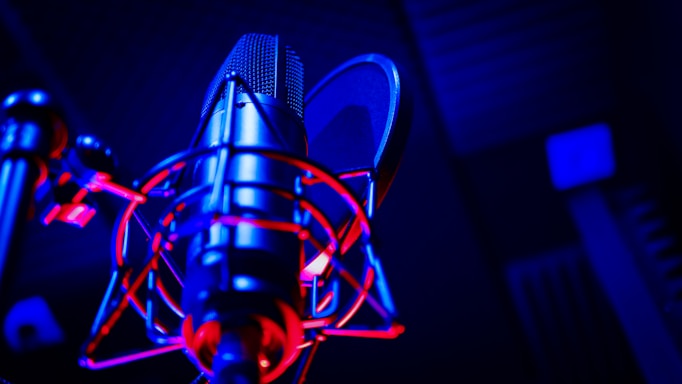 A sleek, dark-themed studio microphone illuminated by neon blue and pink lights.