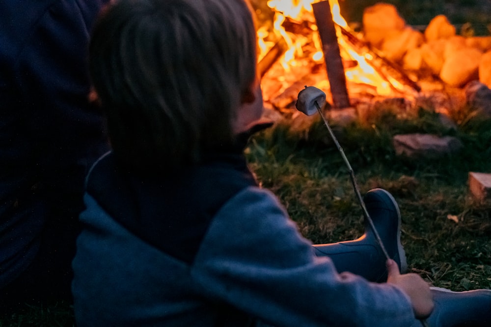 a little boy sitting in front of a campfire