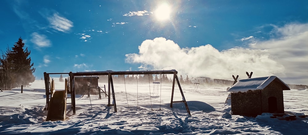 a snow covered field with a swing set and a dog house