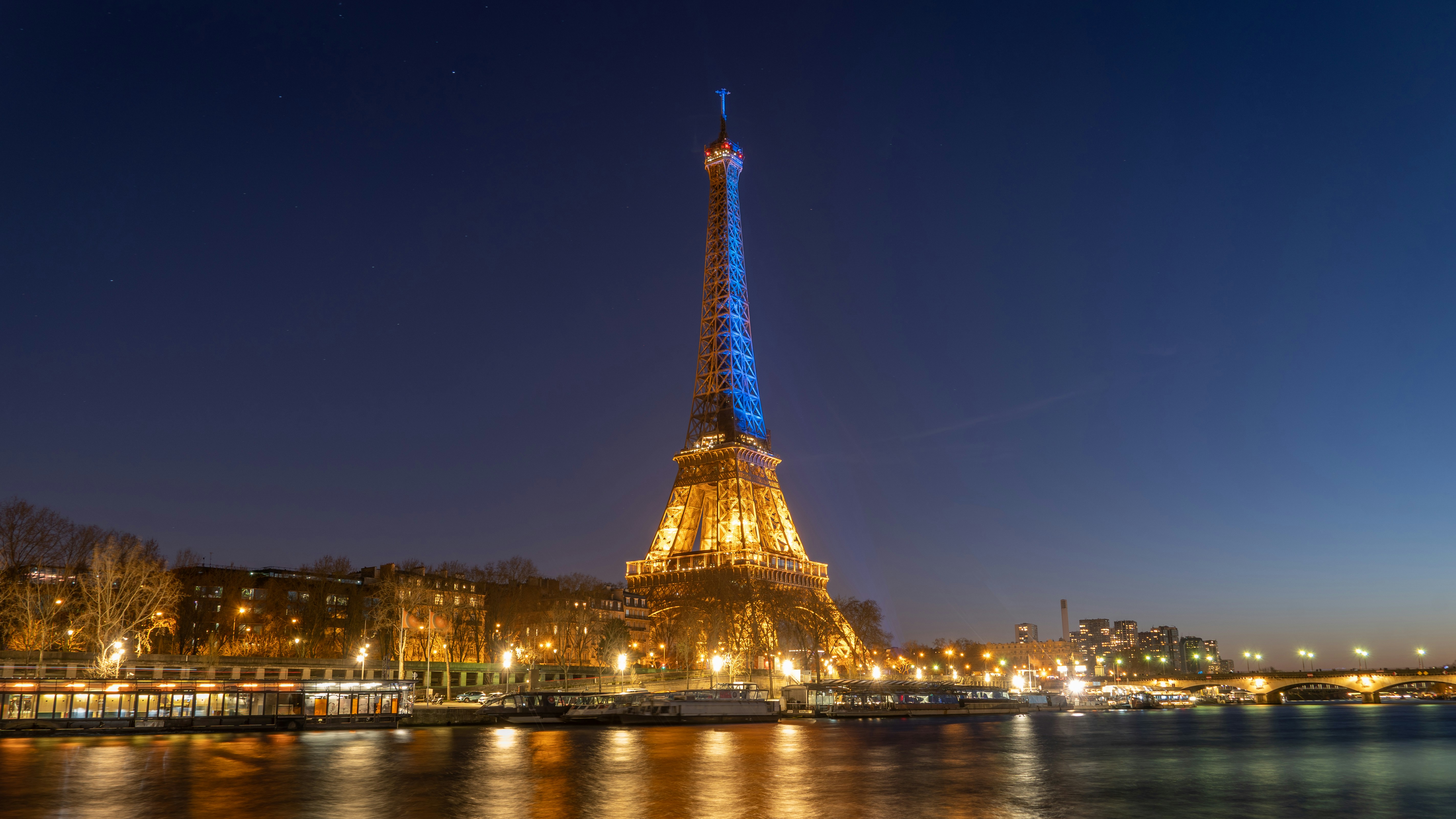 Tour Eiffel illuminée la nuit, lumières dorées sur la Seine, ciel sombre bleu