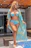 A smiling woman standing next to her newly remodeled pool and patio area under a clear blue sky.
