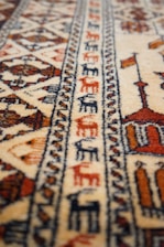 A patterned carpet with intricate geometric designs and earthy tones, featuring detailed motifs and repetitive patterns. The texture appears soft, and the craftsmanship suggests a traditional or cultural style.