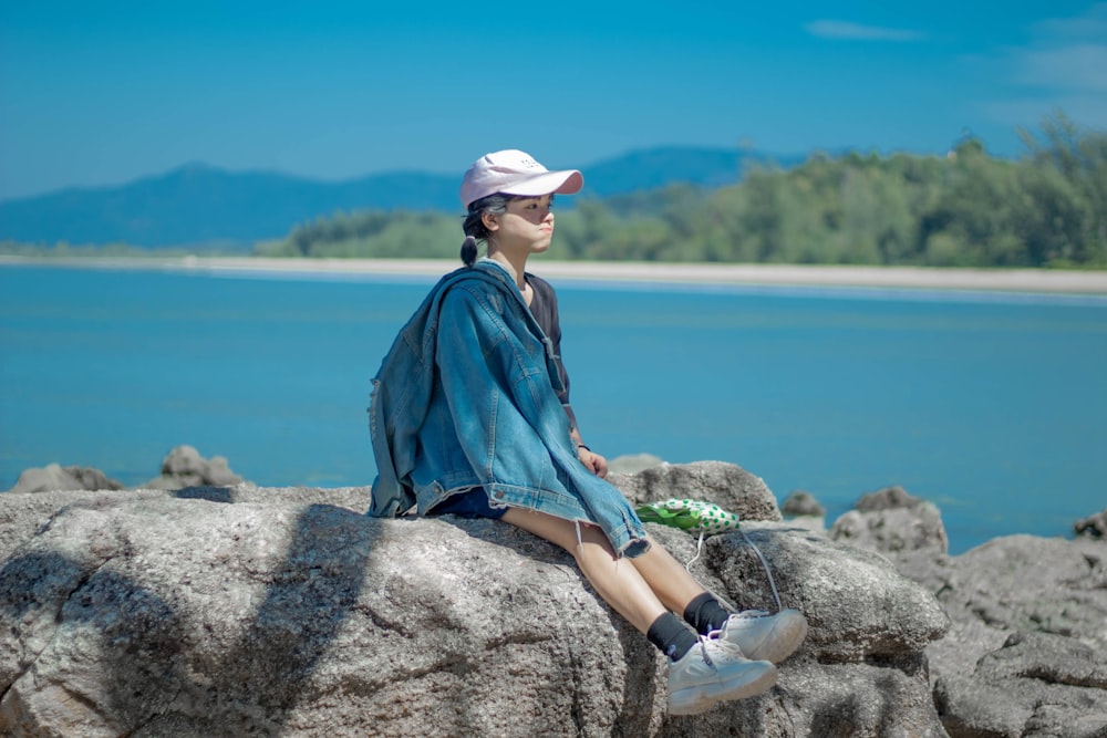 a woman sitting on top of a rock next to a body of water