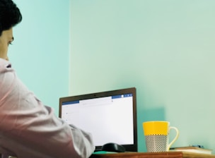 A friendly person sitting at a desk with a laptop, a cup of coffee, and a small flag icon showing English and Spanish.