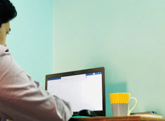A cheerful person browsing deals on a laptop with a bright orange coffee mug nearby.