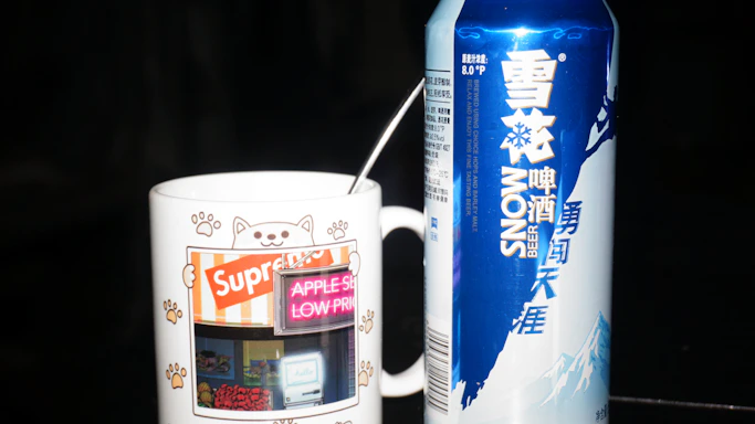 A grumpy black and white cat illustration on a ceramic mug next to an oversized black t-shirt.