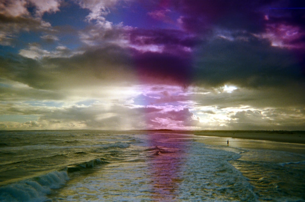 a person walking on a beach under a cloudy sky