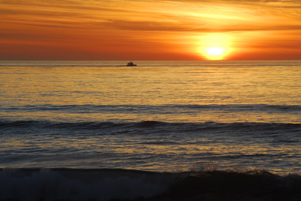 El sol se está poniendo sobre el océano con un bote en la distancia