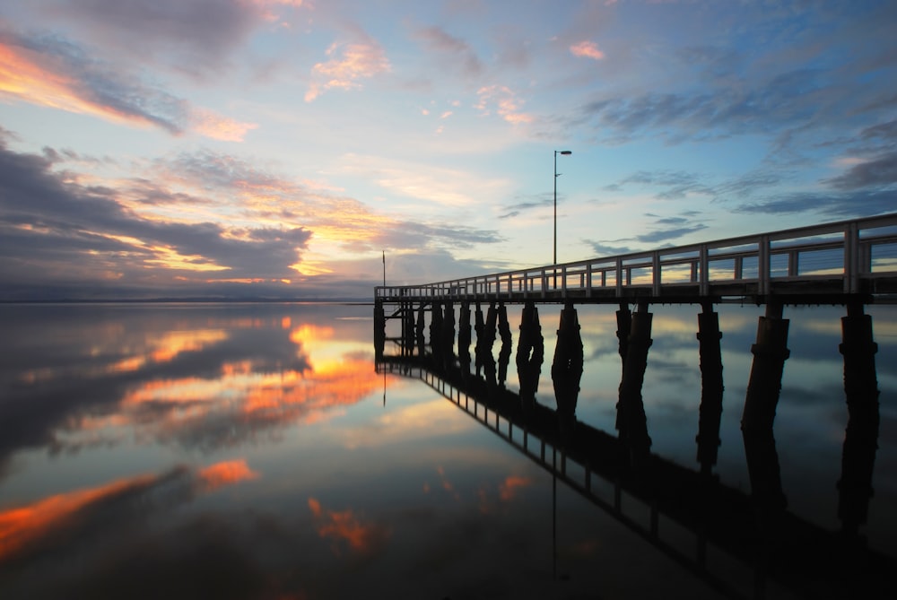 a long wooden pier sitting on top of a lake under a cloudy sky