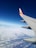 An airplane wing with a distinct orange and white logo is visible against a backdrop of clear blue sky and a layer of fluffy white clouds below.