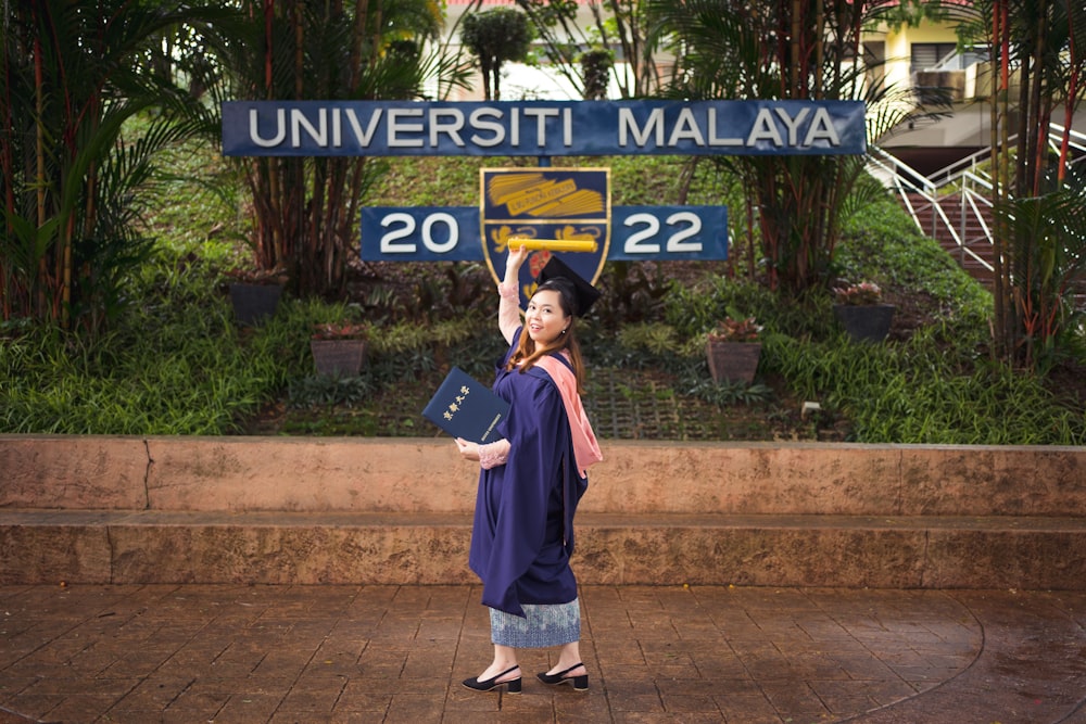 a woman in a graduation gown standing in front of a sign