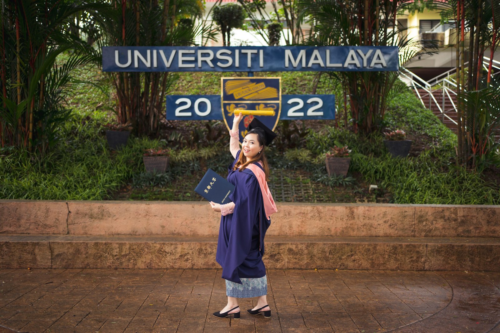 Graduan berjubah akademik di hadapan papan tanda Universiti Malaya, Kuala Lumpur