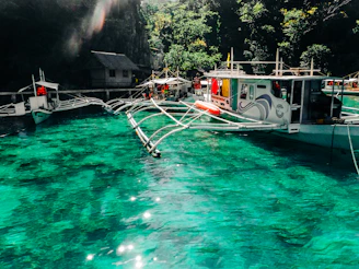 A vibrant outrigger boat gliding through crystal-clear turquoise waters around Caramoan's limestone cliffs.