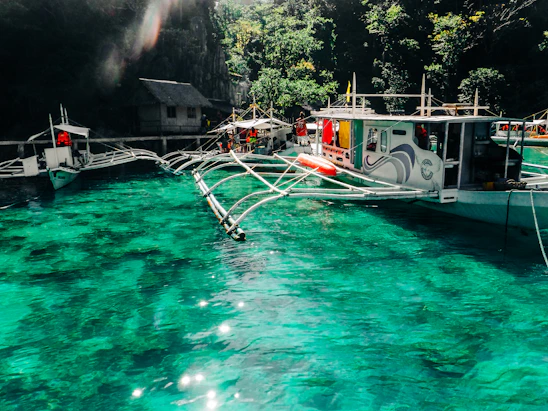 A vibrant outrigger boat gliding through crystal-clear waters with lush Caramoan islands in the background under a bright blue sky.