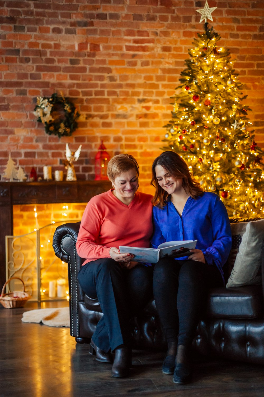 two women sitting on a couch in front of a christmas tree