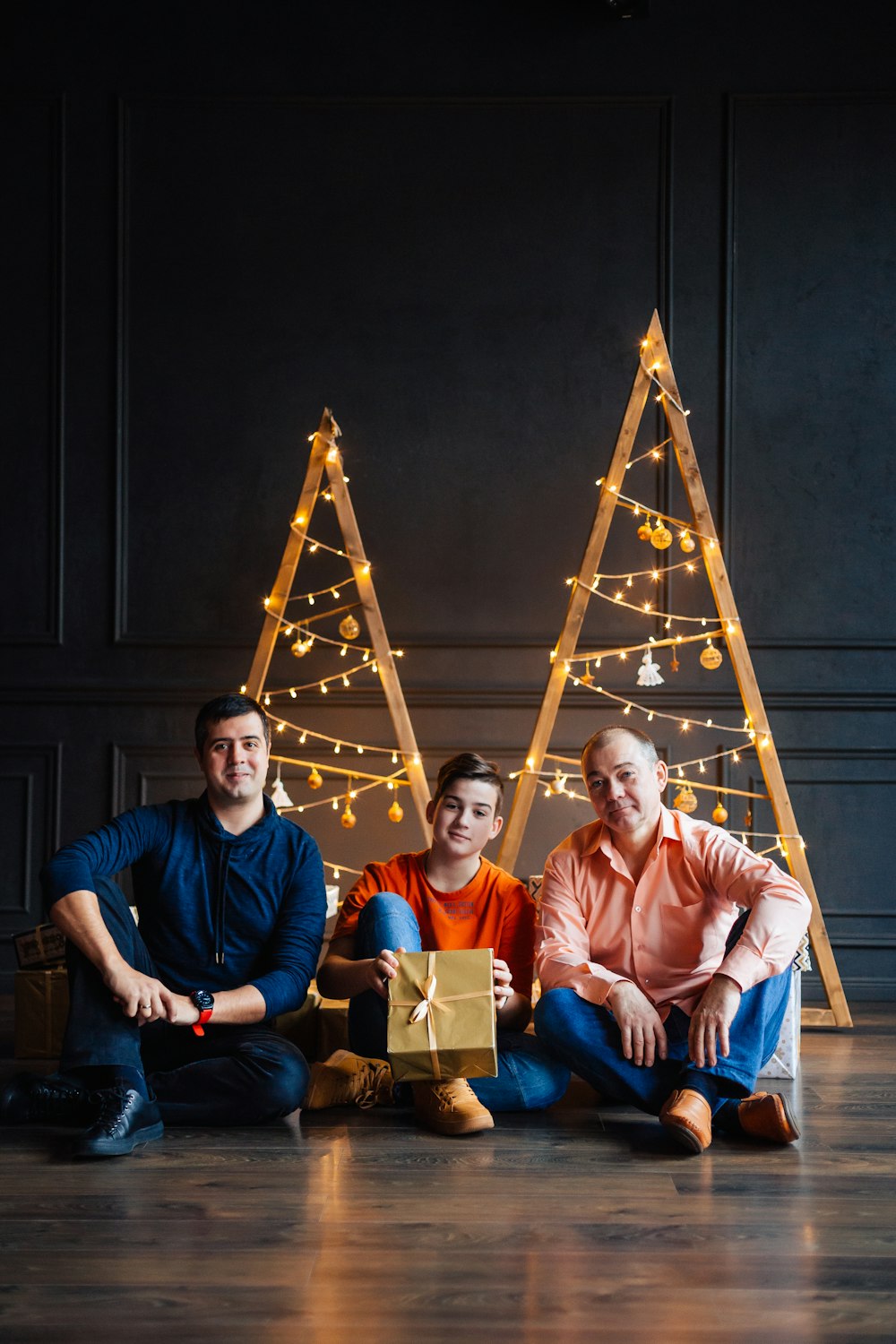 three people sitting on the floor in front of christmas trees