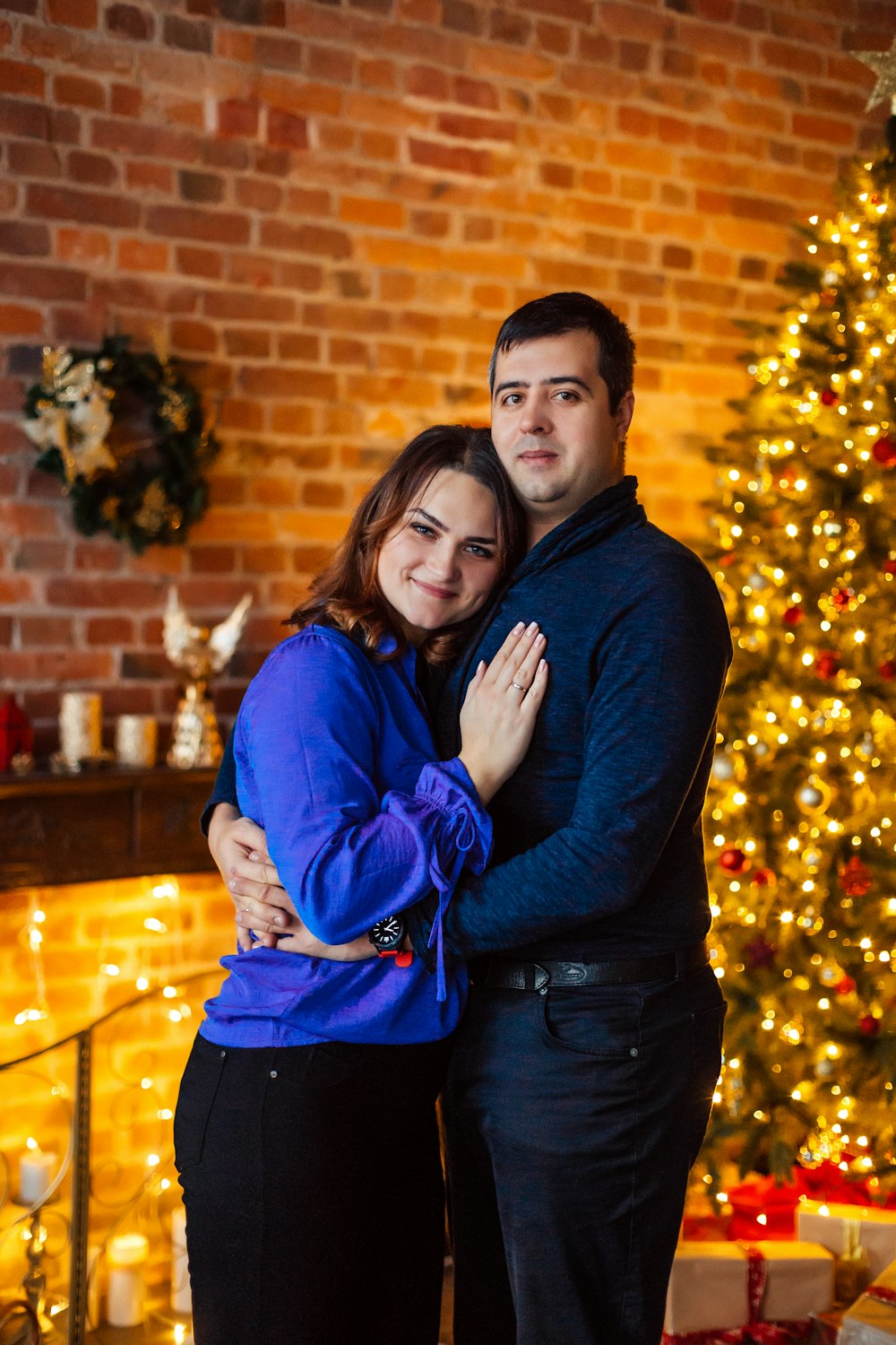 a man and woman hugging in front of a christmas tree