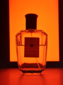 Close-up of Rayhan perfume spray releasing a fine mist into the air against a blurred floral background.