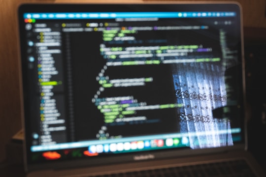 Abstract neon gradient shapes surrounding a laptop showing code updates on screen.