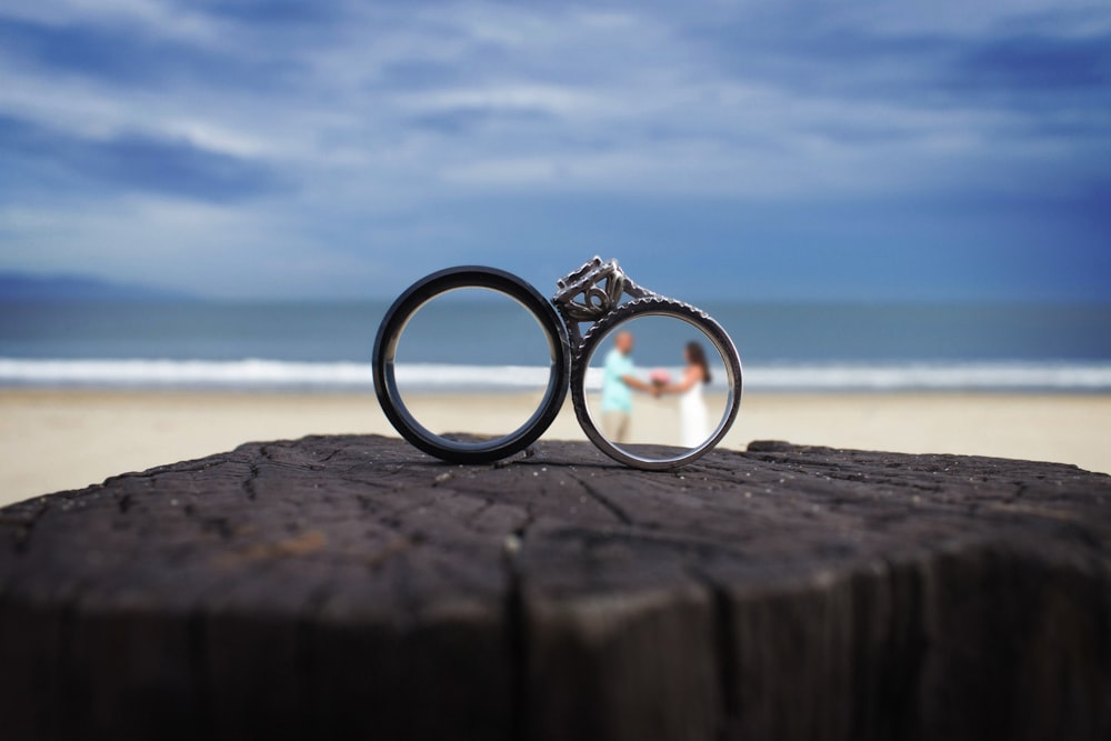 duas alianças de casamento sentadas em cima de um pedaço de madeira