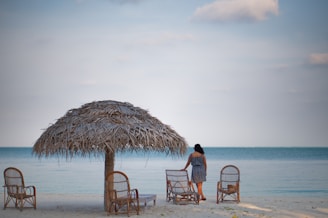 a woman standing under a straw umbrella on a beach