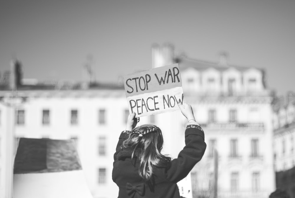 a woman holding a sign that says stop war peace now