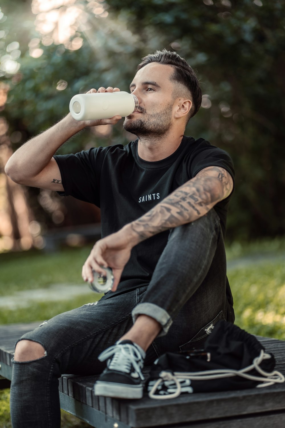 a man sitting on a bench drinking from a bottle