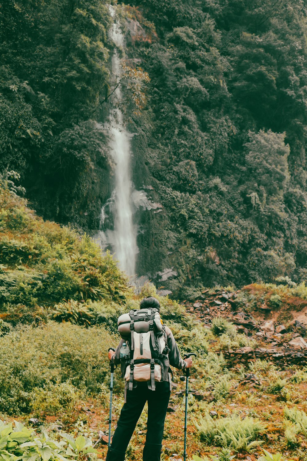 a man with a backpack standing in front of a waterfall
