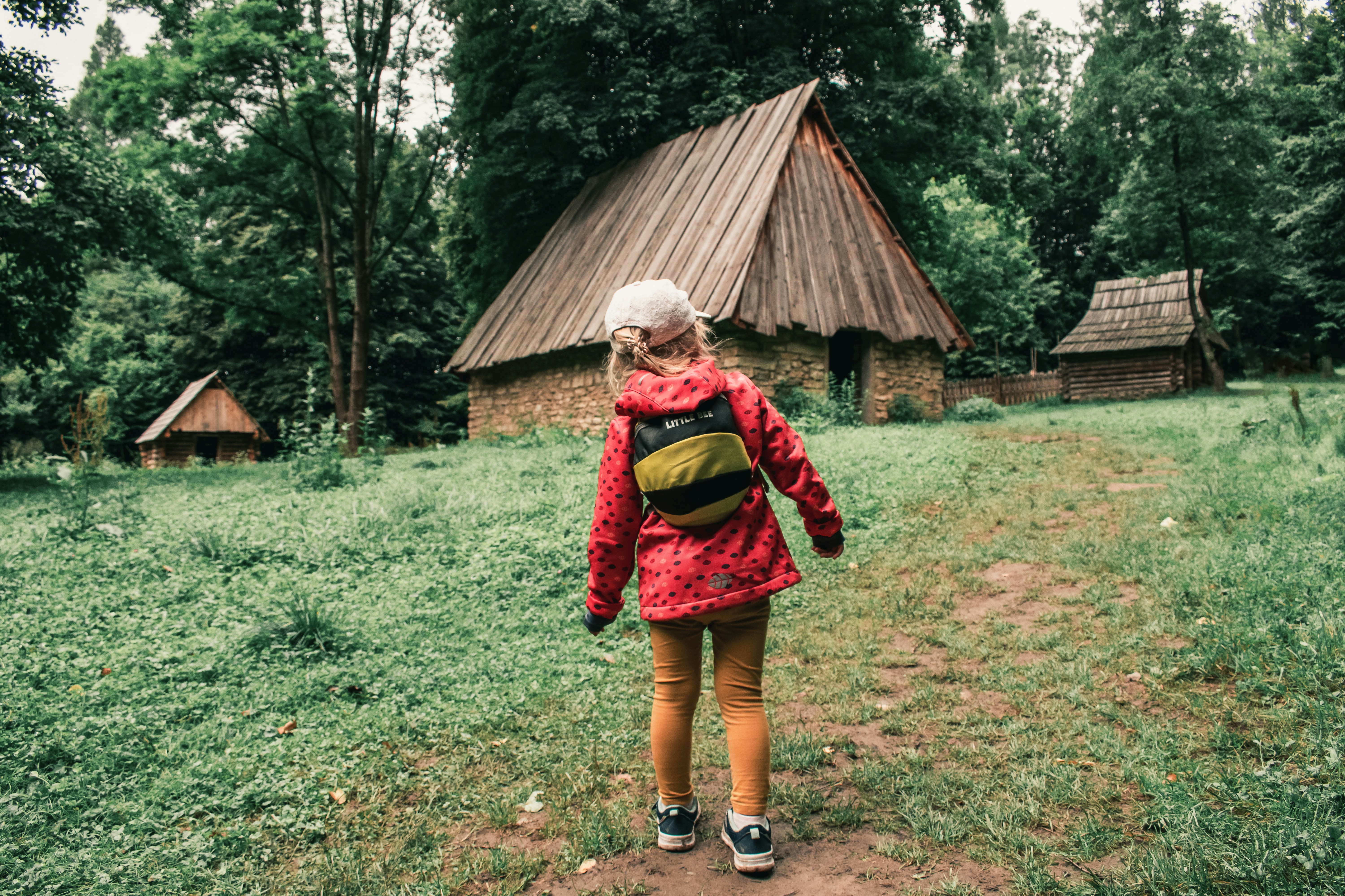 a girl in a red jacket is walking towards a hut, 
