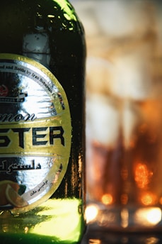 Close-up of a glass bottle filled with golden lemon essential oil surrounded by fresh lemons and green leaves.