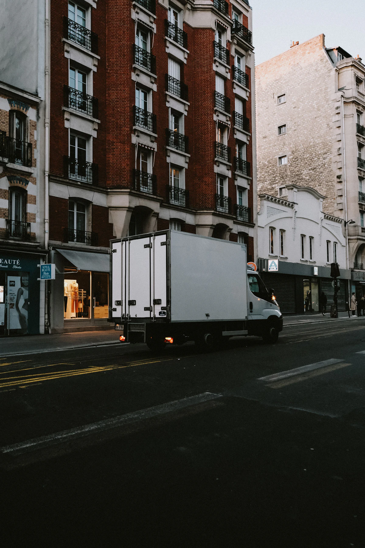 A moving truck driving through a city street between tall buildings