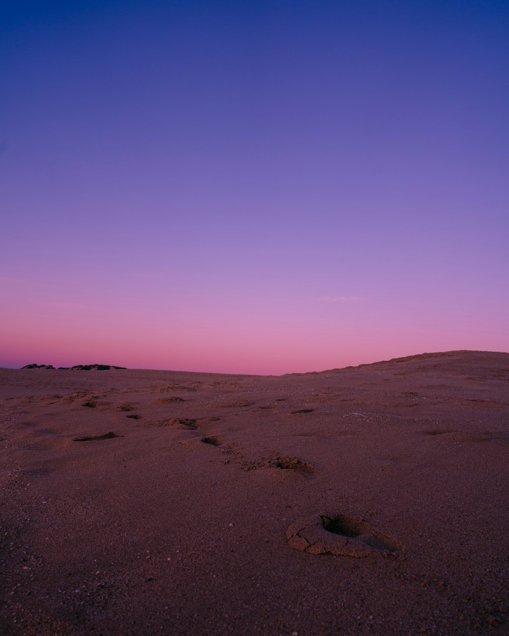 a purple and blue sky with footprints in the sand