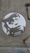 A monochrome stencil art piece featuring a face with an expressive look on a rough, textured wall. The image includes the text 'pa VI niste normalni.'