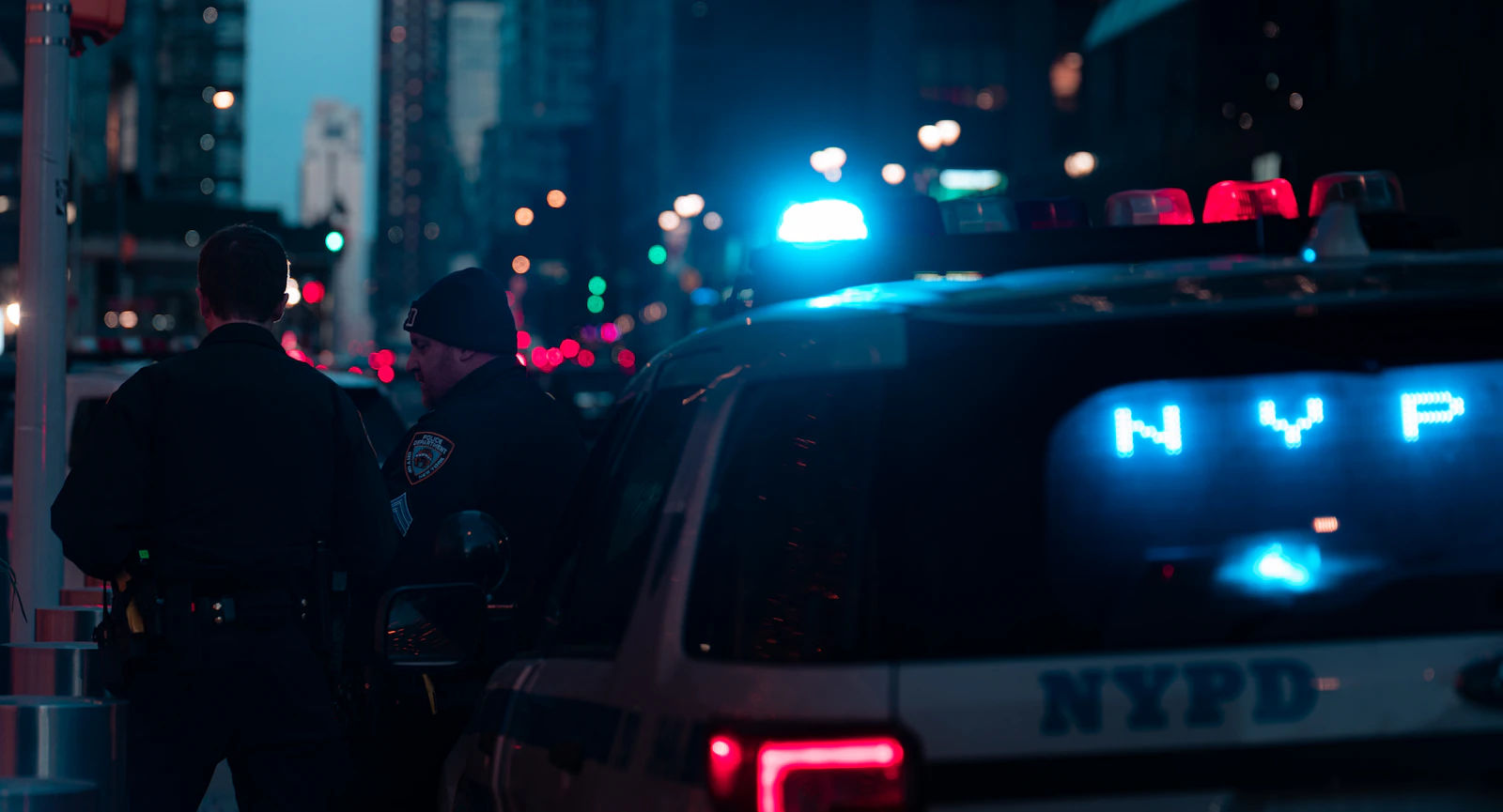 Two NYPD officers beside a police vehicle on a New York street.