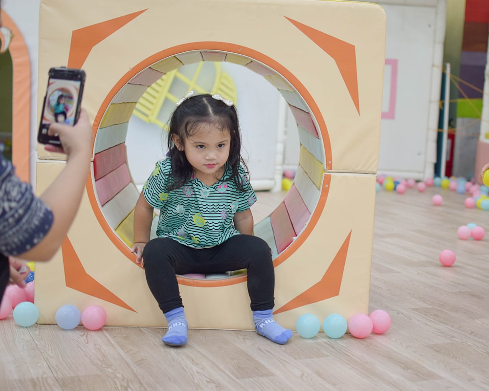 a little girl sitting on a cube in front of a camera