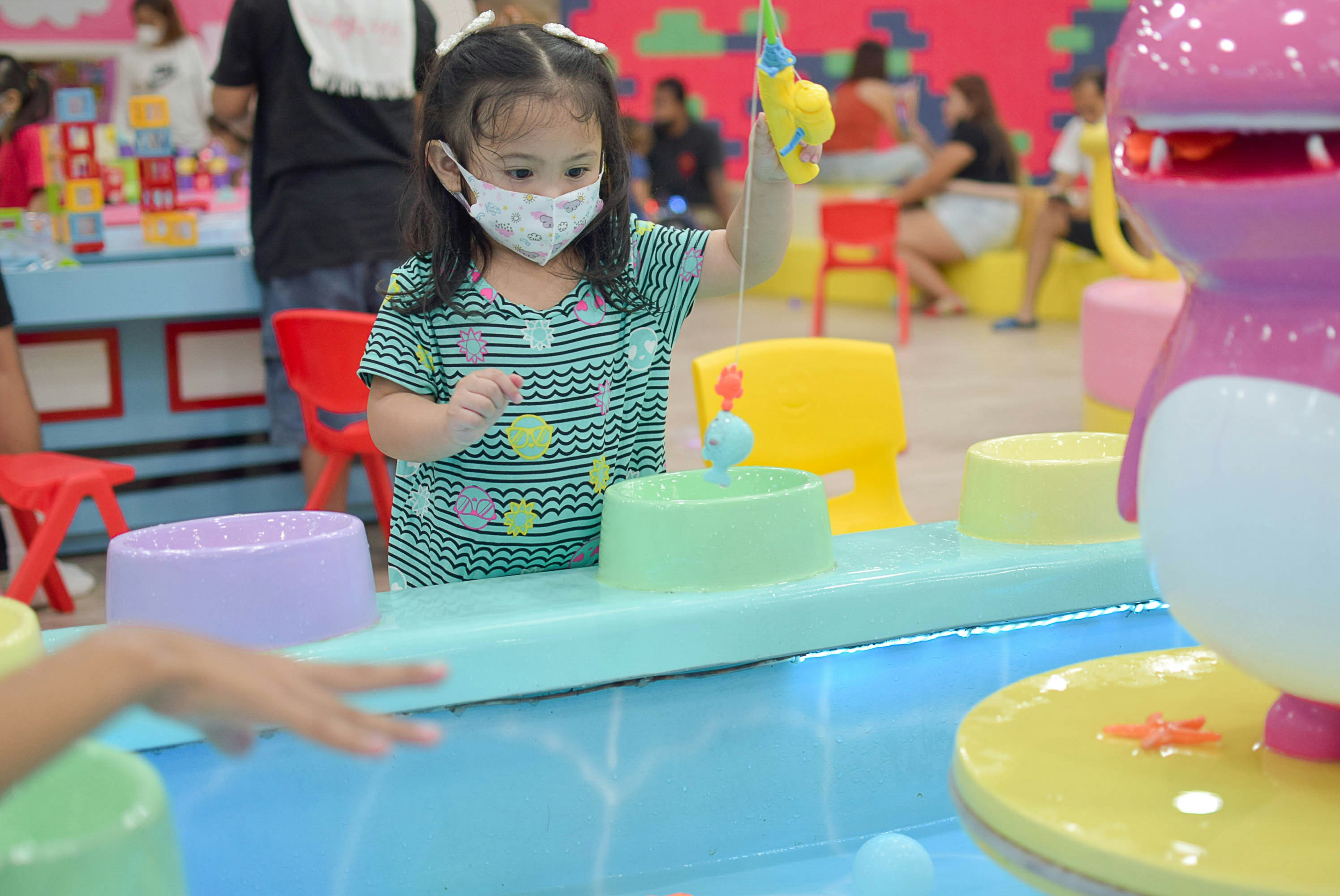 a little girl wearing a face mask standing in front of a table