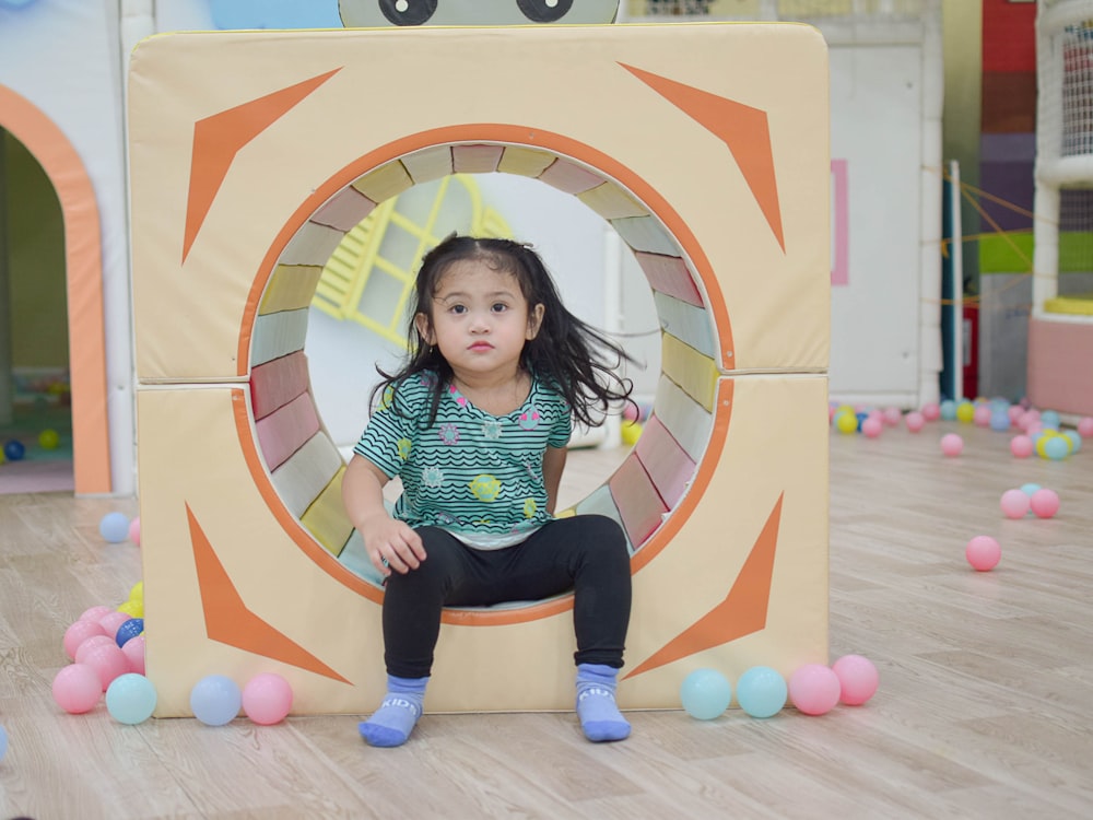 a little girl sitting on a cube in a play room