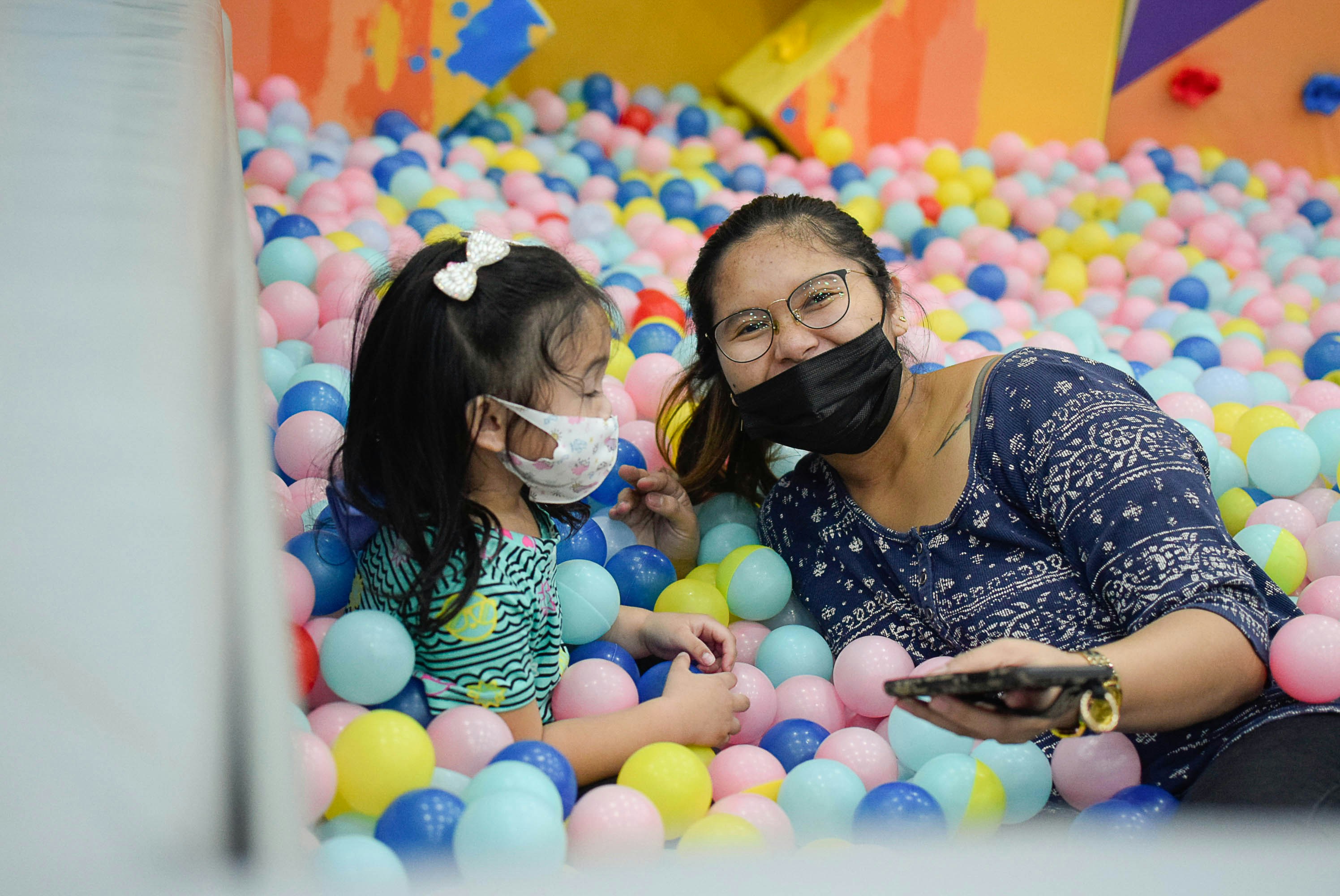 Toddler laughing and diving into a vibrant pit of colourful crush-proof ocean balls — bright cheerful playroom background