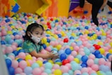 a little girl in a ball pit with a mask on