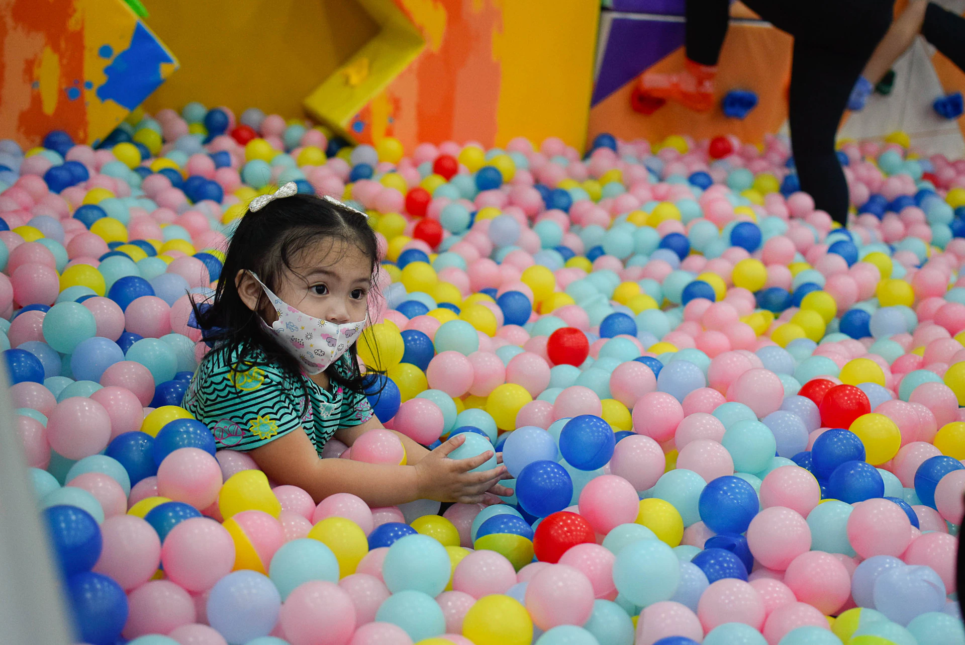 a little girl in a ball pit with a mask on