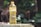 A plastic bottle filled with cooking oil is placed outdoors on a stone or concrete surface. The label on the bottle reads 'HEMART', with additional text. The background consists of out-of-focus greenery, including leaves and possibly tree trunks.