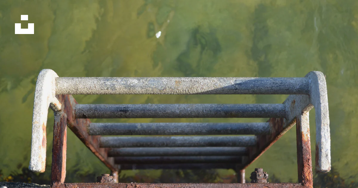 A rusted metal bench sitting next to a body of water photo – Free Grey ...