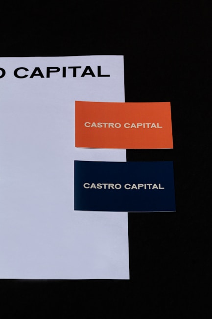Two business cards placed on a white sheet. The cards are orange and dark blue, each with the text 'CASTRO CAPITAL' printed in uppercase.