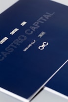 A close-up of a sleek dark blue cover design featuring text in white and light gray, including 'CASTRO CAPITAL .COM', 'SAN LUIS, S.L.P.', and a number '78214'. The design includes a stylized logo with interlocking letters.