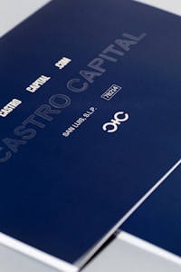 A close-up of a sleek dark blue cover design featuring text in white and light gray, including 'CASTRO CAPITAL .COM', 'SAN LUIS, S.L.P.', and a number '78214'. The design includes a stylized logo with interlocking letters.