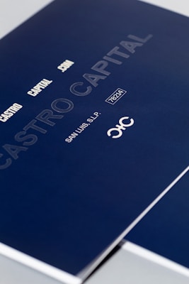 A close-up of a sleek dark blue cover design featuring text in white and light gray, including 'CASTRO CAPITAL .COM', 'SAN LUIS, S.L.P.', and a number '78214'. The design includes a stylized logo with interlocking letters.